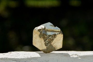 Pyrit Würfel im Sonnenlicht, auf weißer Mauer mit dunkelgrünem Hintergrund