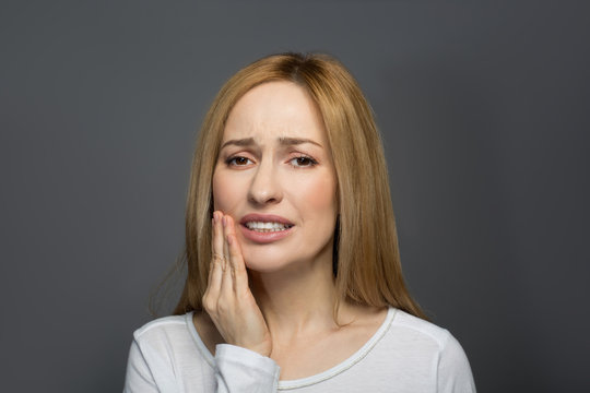 Dental treatment. Portrait of joyless female holding her hand on cheek and wincing in pain. Isolated on background