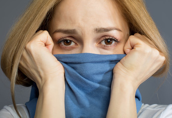 Close up of blonde woman covering her mouth with scarf, her eyes expressing sadness. Isolated on background