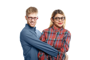 People, relationships, love, romance and dating concept. Picture of beautiful blonde woman having disgusted look while being held tight by weird unshaven nerdy male against white wall background