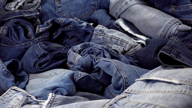 A pile of trendy blue jeans pants on a wooden background. HD video clip
