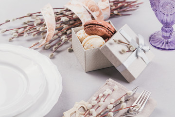 White plate, purple glass, cutlery, present box with macaroons and pussy willow twigs