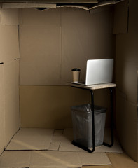 Little space concept. Empty cramped cardboard office with small table and modern laptop on it