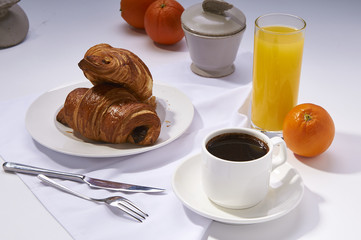 Fresh croissants, orange juice, coffee and oranges. Continental breakfast on white table