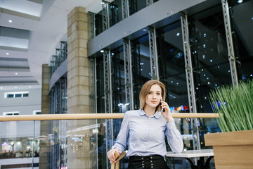 A young woman talking through the phone. The girl is sitting at the table and makes an order. Business woman