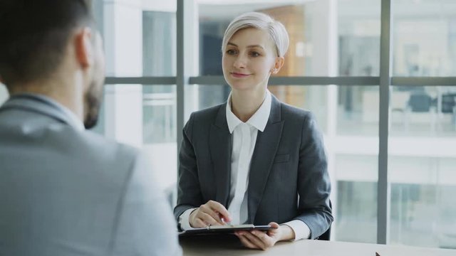 HR businesswoman having job interview with young man in suit and watching his resume application in modern office