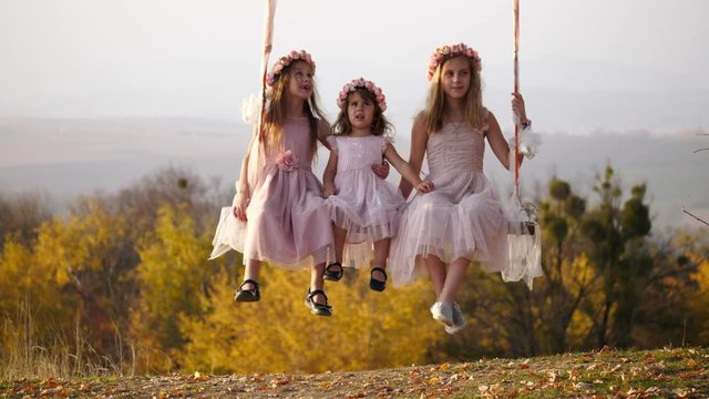 Three beautiful little girls swinging on a swing under a big tree.