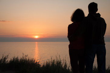 Romantic couple meets the sun rising above the sea surface.
