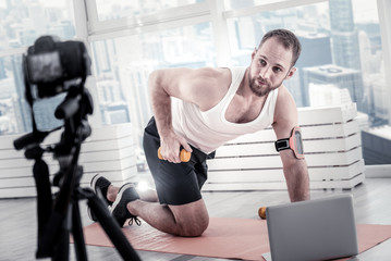 Be attentive. Adorable nice male blogger recording video and working with dumbbell while working out back