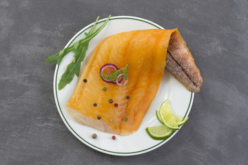 beautiful yellow smoked haddock fish fillet on a plate with a branch of fresh arugula, lime and pink berry on grey slate background