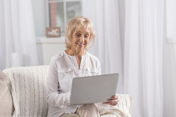 Worldwide web. Beautiful positive mature woman holding laptop while smiling and looking at screen