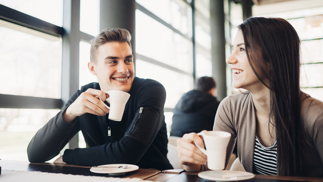 Cheerful couple enjoying coffee together in modern cafe.Drinking hot caffeine beverage on a break with business partner.Friend meeting for coffee downtown.Smiling happy people.Funny conversation