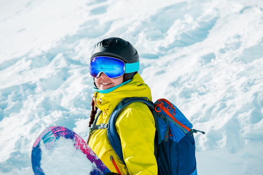 Portrait of smiling woman in helmet and with snowboard on background of snowy landscape