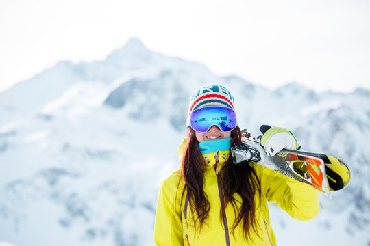 Photo of woman in mask with skis on her shoulder against background of snowy hill