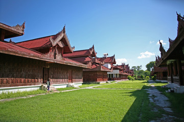 Fototapeta premium A young backpacker walks beside the beautiful historical wooden buildings within the central palace complex of the Mandalay citadel in Burma
