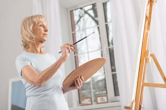 I change this. Glad appealing mature woman staring at easel while posing in profile and rising tassel