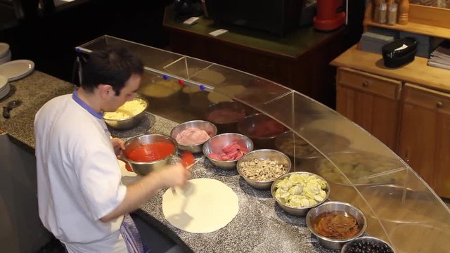 italian pizzaiolo spreading pasteurized tomato paste and spreading toppings on pizza