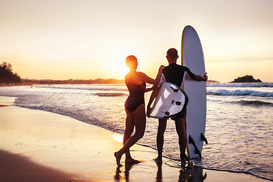 Couple surfers stay on sunset ocean beach