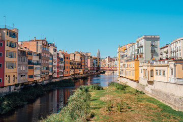 Naklejka na ściany i meble Colorful yellow and orange houses and bridge Pont de Sant Agusti reflected in water river Onyar, in Girona, Catalonia, Spain.