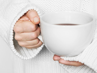Warming cup of tea in the hands of woman in white sweater.