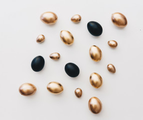 Black and gold eggs over white background. Minimal flat lay