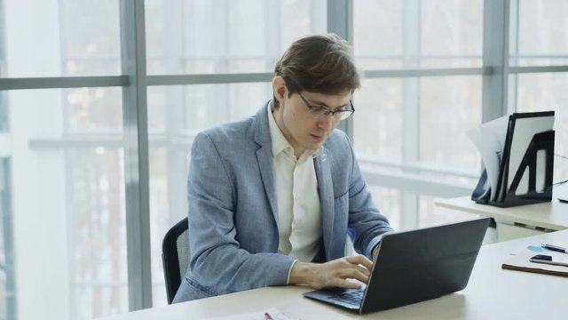 Young businessman using laptop computer receiving good message and become very excited and happy sitting in modern office
