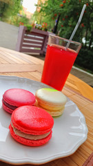 макаруны на тарелке с красным морсом в летнем кафе на фоне зелени 