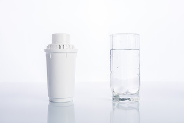 Replacement water filter and glass of purified water on white background, reflection