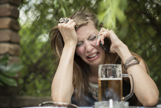 Heart broken girl crying over her cellphone, drunk, drinking a beer in a bar