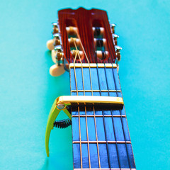 Golden capo on acoustic guitar neck on blue background. Musical instrument equipment. Simple music...