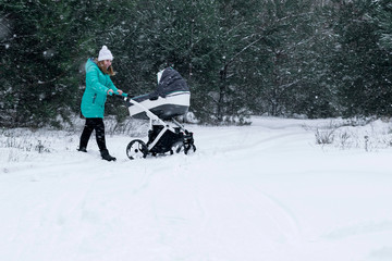 Young beautiful mother walking with stroller in city park at winter. Happy motherhood concept. Enjoying carefree maternity. Free space for text.