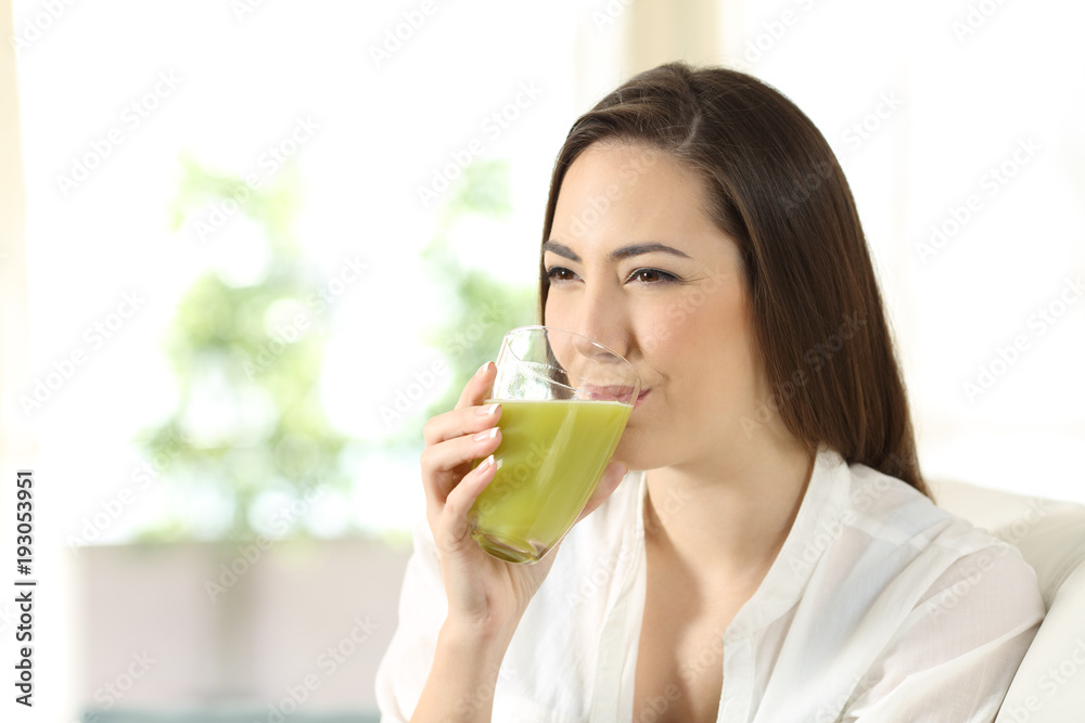 Wall mural Woman drinking a green vegetable juice at home