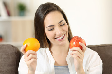 Woman deciding between orange and apple at home