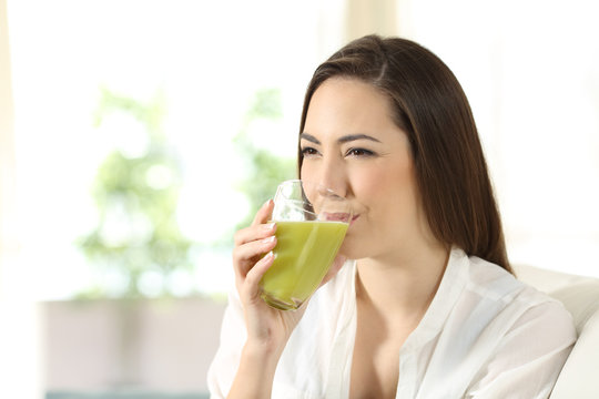 Woman drinking a green vegetable juice at home