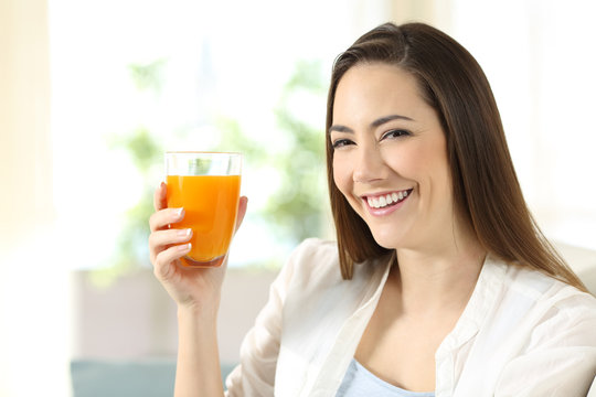 Woman holding a glass of orange juice looking at you