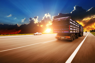 Rear view of the big truck driving fast with trailer on the countryside road against night sky with sunset