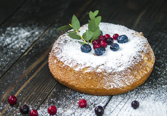 Sponge cake with berry and sugar powder on dark wooden background