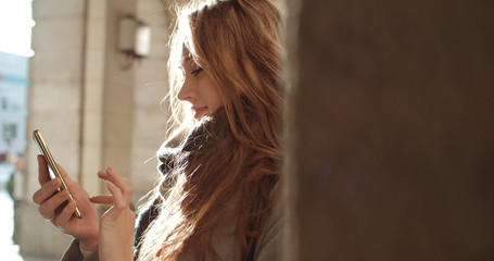 Fototapeta premium Beautiful young woman typing on phone during sunny day.