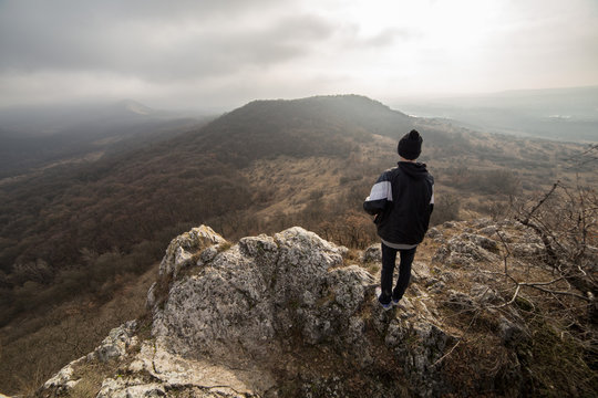 Wide angle panorama from a cliff on the top of a mountain with young man in back light sky.
