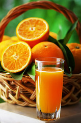 glass with juice and oranges on  basket