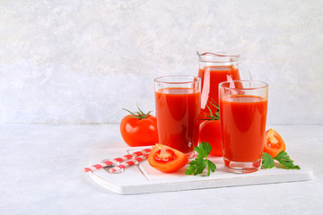 Tomato juice in glasses and a pitcher on a gray concrete table.