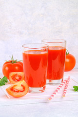 Tomato juice in glasses on a gray concrete table.