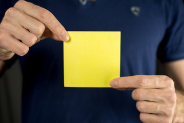 Man holds blank yellow sticker. Thumb up, blue T-shirt. close-up, selective focus