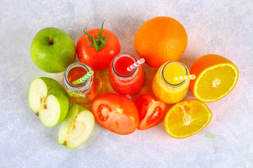 Bottles with fresh orange, apple, tomato juice and colored tubules on a gray concrete table. Top view.