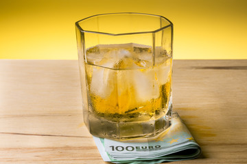 Glass of whiskey on a hundred euro banknote in the center of the frame.