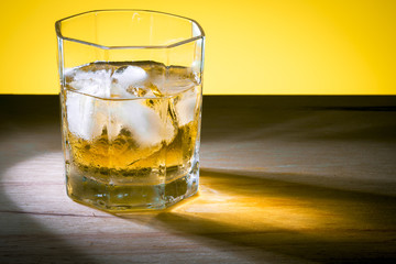 Glass of whiskey in the left corner of the frame with a side light coming from the left.