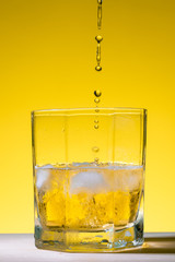 Whiskey being served in a glass with ice on a yellow background