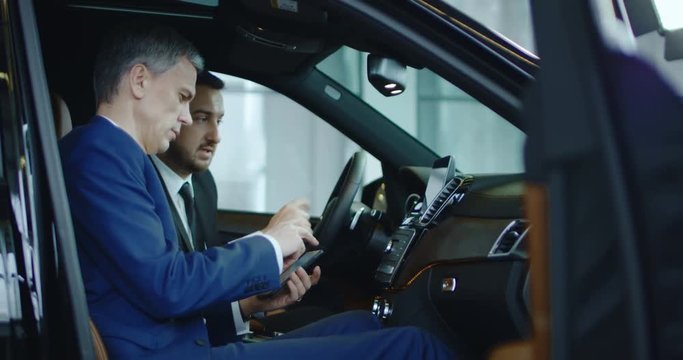 Side view of manager and businessman connecting smartphone to car computer in showroom.