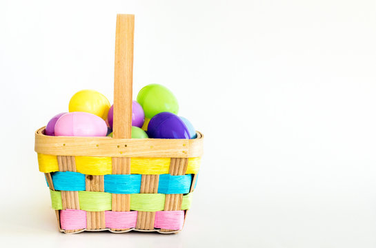 wicker Easter basket with colorful weaved ribbons filled with plastic Easter eggs isolated on white