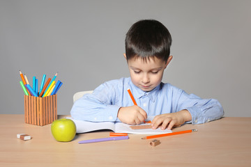 Cute little boy doing homework against grey background